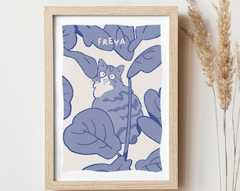 May include: A framed print with a blue and white illustration of a cat hiding in a leafy plant. The text "FREYA" is written above the cat.