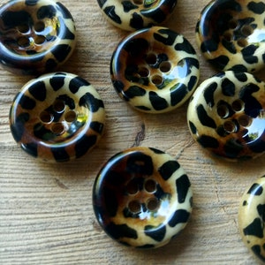 Puede incluir: Un conjunto de ocho botones de estampado de leopardo marrón y negro con cuatro agujeros cada uno.