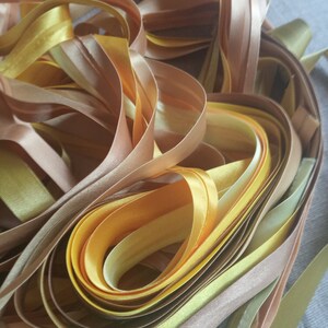 May include: A pile of satin ribbon in shades of yellow, gold, and brown. The ribbon is arranged in a loose, flowing pattern.