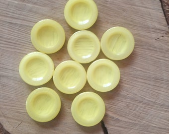 May include: Nine yellow round buttons with a raised center and a subtle striped pattern. The buttons are arranged in a star shape on a wooden surface.