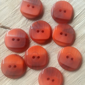 May include: Nine orange plastic buttons with two holes each. The buttons have a textured, striped design.