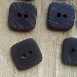 Peut inclure: Six boutons carrés avec deux trous chacun. Les boutons sont de couleur violet foncé avec un motif marbré.