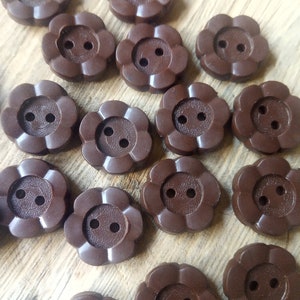 Może przedstawiać: Zbiór brązowych plastikowych guzików w kształcie kwiatów z dwoma otworami każdy. Guziki są ułożone w przesunięty wzór na drewnianej powierzchni.