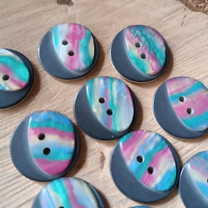 Op de afbeelding: Een verzameling van tien kleurrijke, twee-gaats knopen met een zwarte achtergrond. De knopen hebben een draaiende print van roze, blauw en groen.