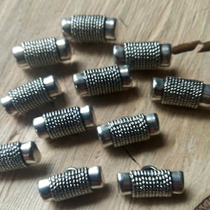 Pode incluir: Dez botões de metal prateados com um design texturizado. Os botões são de forma cilíndrica e têm uma borda ligeiramente arredondada.