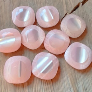 Può includere: Otto bottoni quadrati rosa con un centro rotondo, iridescente e rialzato. I bottoni hanno un design sottile e testurizzato.