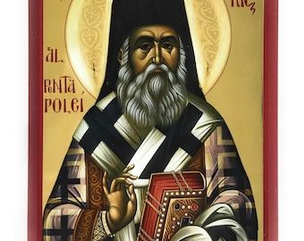 May include: A hand-painted icon of Saint Nectarios of Pentapolis, a Greek Orthodox saint. The icon depicts him in a black cassock and white robes, holding a book. The background is gold with a halo around his head. The text "Necta Rie" is written in the upper right corner.