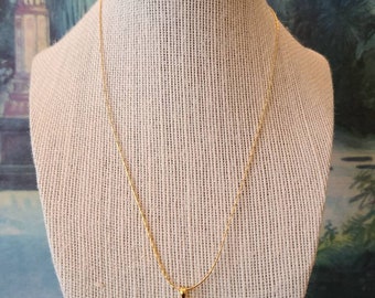May include: A gold chain necklace with a gold evil eye pendant. The pendant has a green stone in the center.