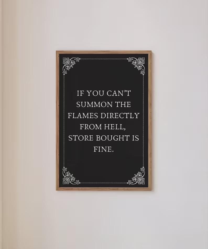 May include: Black chalkboard with a white frame and white decorative flourishes in the corners. The text on the chalkboard reads: "IF YOU CAN'T SUMMON THE FLAMES DIRECTLY FROM HELL, STORE BOUGHT IS FINE."