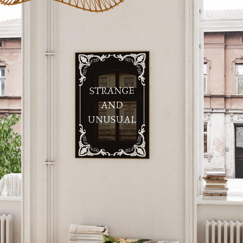 May include: Black and white framed sign with the text "STRANGE AND UNUSUAL" in a decorative font.