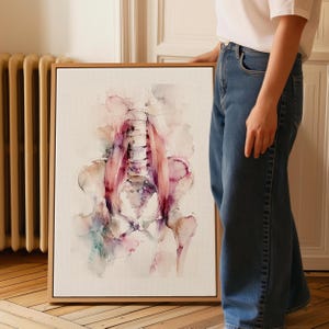 May include: Watercolor painting of a human skeletal structure, including the spine and pelvis, in shades of pink, purple, and beige. The artwork is framed in a natural wood frame, creating a modern aesthetic. The painting is displayed against a neutral background.