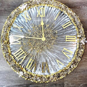 May include: A round wall clock with a gold and crystal encrusted border. The clock face has a white and gray marbled design with gold Roman numerals and hands. The clock measures approximately 18 inches in diameter.