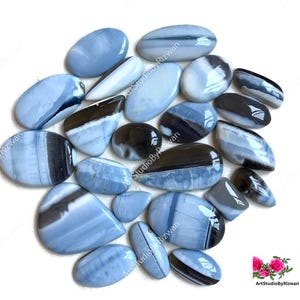 May include: A collection of polished, oval-shaped gemstones in shades of blue, white, and black. The stones vary in size and have a smooth, glossy finish. The arrangement suggests a focus on natural stone jewelry or craft supplies.