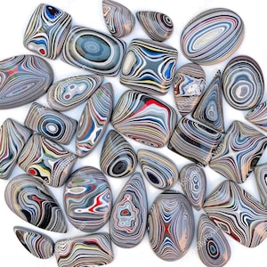 May include: A collection of colourful, polished, agate stones with intricate patterns. The stones are various shapes and sizes, including oval, round, and teardrop.