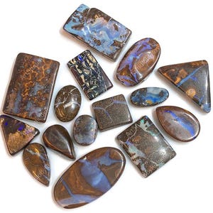 May include: A collection of polished boulder opals in various shapes including rectangles, ovals, triangles, and teardrops. Each stone features a dark brown ironstone matrix with iridescent blue, purple, and gold flashes of color throughout.