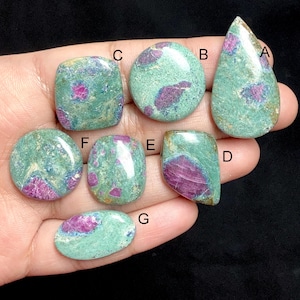 Puede incluir: Colección de siete piedras preciosas de rubí zoisita pulidas en varias formas. Las piedras presentan una mezcla de colores verde turquesa y rojo rosado. Las formas incluyen ovalada, redonda y de lágrima. Las piedras preciosas se muestran sobre un fondo oscuro.