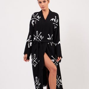May include: A black and white patterned robe with a long, flowing silhouette. The robe has a V-neck and a tie belt. The pattern features a repeated design of crossed swords and other symbols.
