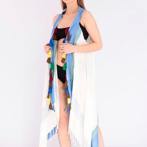 May include: White beach cover-up with blue and green stripes and colorful tassels. The cover-up is made of a lightweight fabric and has a relaxed fit.