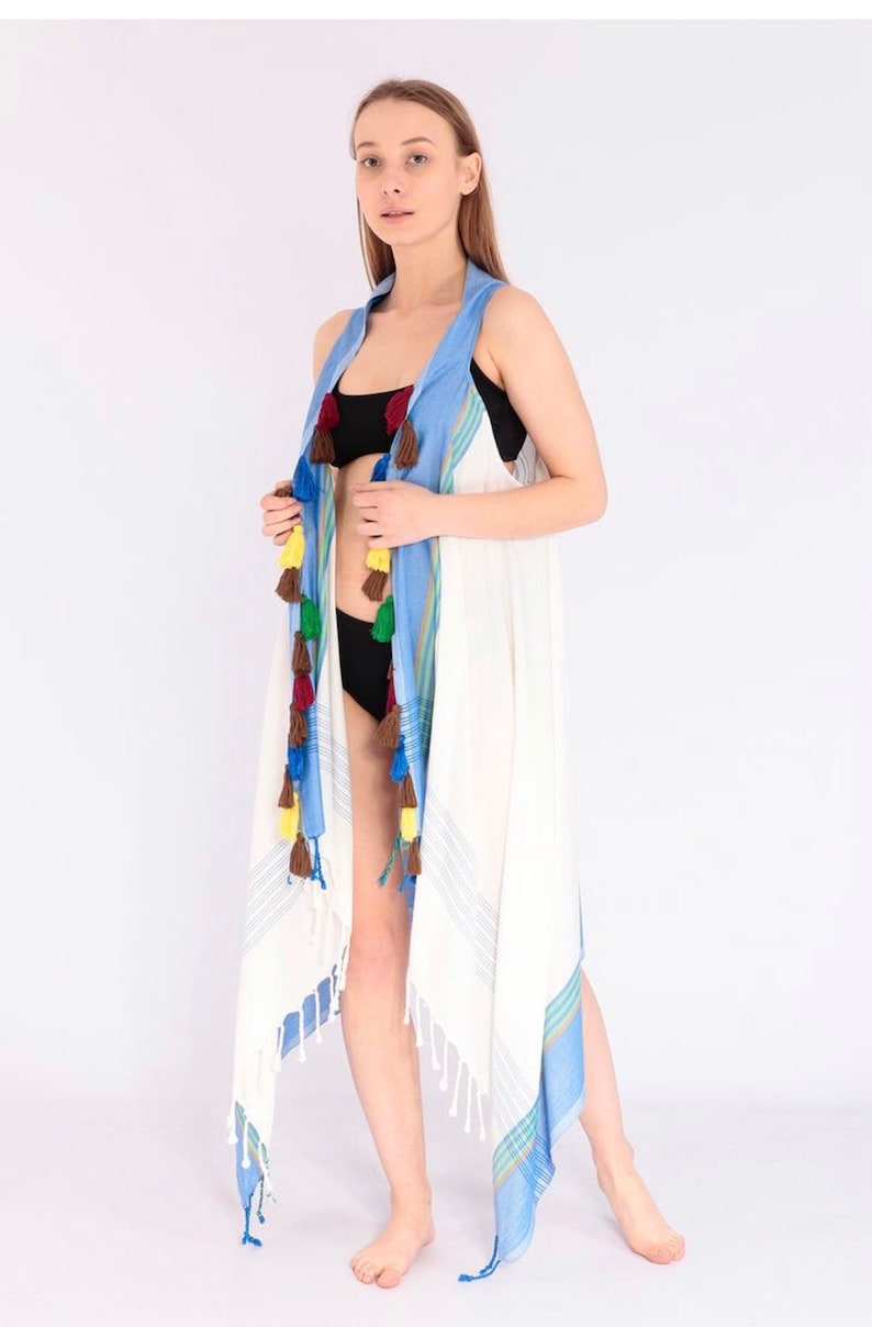 May include: White beach cover-up with blue and green stripes and colorful tassels. The cover-up is made of a lightweight fabric and has a relaxed fit.