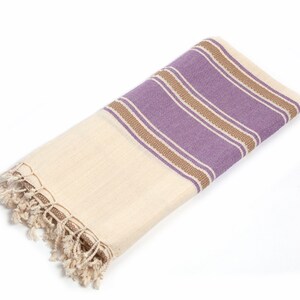 Peut inclure: Une serviette en coton blanc avec des rayures violettes et brunes et une bordure en franges.