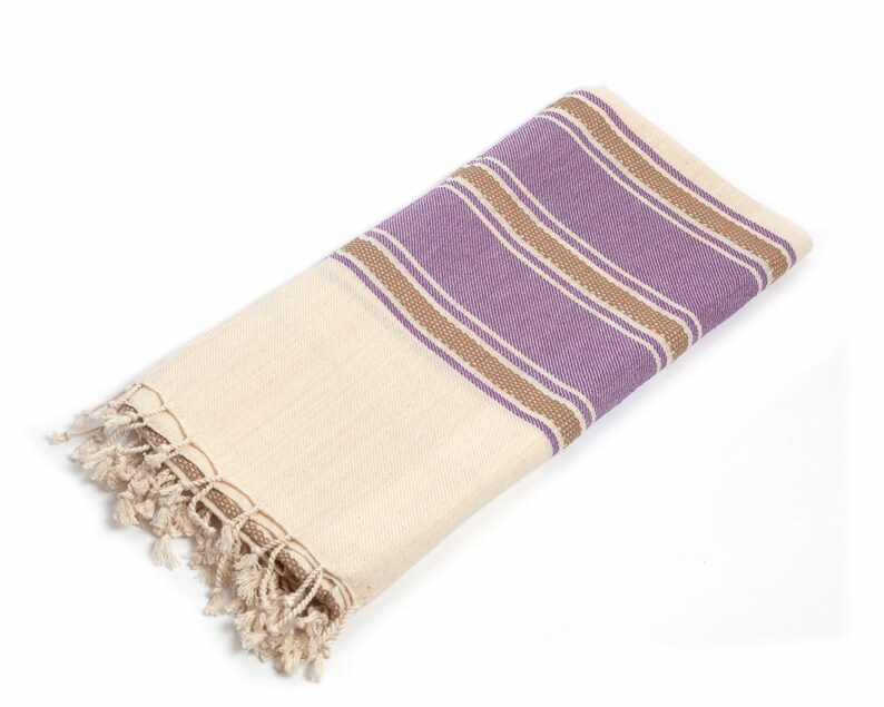 Peut inclure: Une serviette en coton blanc avec des rayures violettes et brunes et une bordure en franges.
