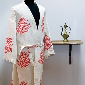 May include: White bathrobe with a coral design. The robe has a tie belt and fringe trim.