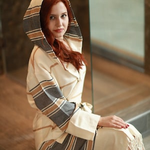 Peut inclure: Une robe blanche &agrave; capuche avec des rayures brunes et grises. La robe a une coupe longue et fluide et est faite d'un tissu doux et confortable.