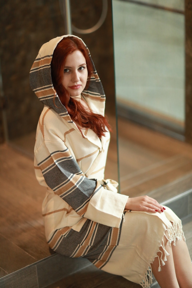 Peut inclure: Une robe blanche &agrave; capuche avec des rayures brunes et grises. La robe a une coupe longue et fluide et est faite d'un tissu doux et confortable.