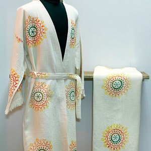 May include: A white cotton robe with a fringed hem and a matching towel. Both are decorated with a repeating pattern of colorful circular designs.
