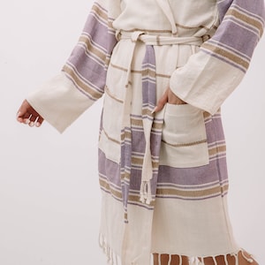 Peut inclure: Une robe blanche et violette &agrave; rayures avec une capuche et une ceinture &agrave; nouer. La robe a une poche sur le c&ocirc;t&eacute; gauche et une bordure en frange autour du bas.