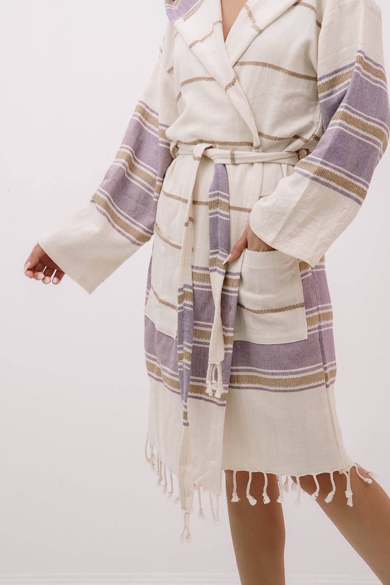 Peut inclure: Une robe blanche et violette &agrave; rayures avec une capuche et une ceinture &agrave; nouer. La robe a une poche sur le c&ocirc;t&eacute; gauche et une bordure en frange autour du bas.