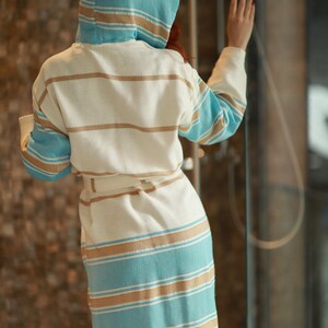 Peut inclure: Une robe blanche &agrave; capuche avec des rayures bleues et brunes. La robe a une ceinture &agrave; nouer et est faite d'un mat&eacute;riau doux et absorbant.