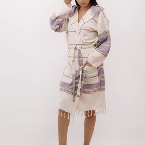 Peut inclure: Une robe blanche &agrave; capuche avec des rayures violettes et brunes. La robe a une ceinture &agrave; nouer et une bordure en franges.