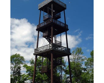 May include: A wooden observation tower with three levels and a staircase. The tower is surrounded by trees and a blue sky with white clouds.
