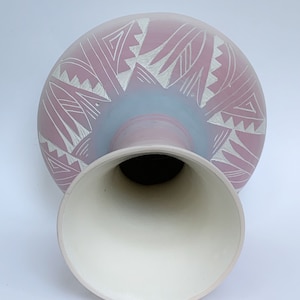 Peut inclure: Un vase en céramique rose et blanc avec un motif géométrique. Le vase a une base large et un col étroit.
