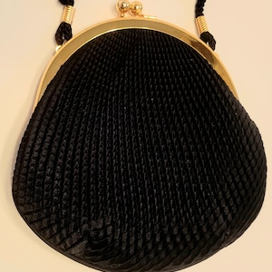 May include: A black, vintage-style purse with a gold-colored frame and clasp. The purse has a textured, pleated design and a black cord handle. The clasp features two small, gold-colored spheres.