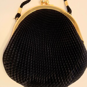 May include: Black evening bag with a textured, pleated design. The bag features a gold-tone frame and clasp, with a braided black strap. The bag's shape is rounded at the bottom and tapers towards the top, creating a classic silhouette.