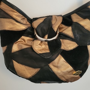 May include: A black and gold patchwork leather handbag with a silver ring handle.