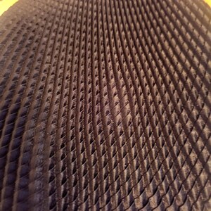 May include: Close-up of a dark navy blue fabric with a quilted, diamond-shaped pattern. The texture creates a sense of depth and dimension, with the light reflecting off the raised areas. The fabric appears to be soft and luxurious.
