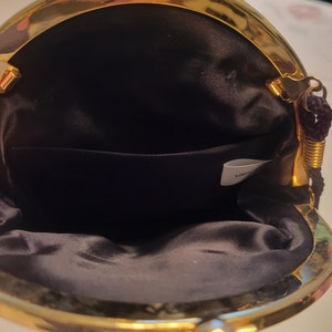 May include: Open view of a small, black satin purse with a gold-colored metal frame. The purse has a kiss-lock closure and a small interior pocket. A black cord handle is attached to the frame.