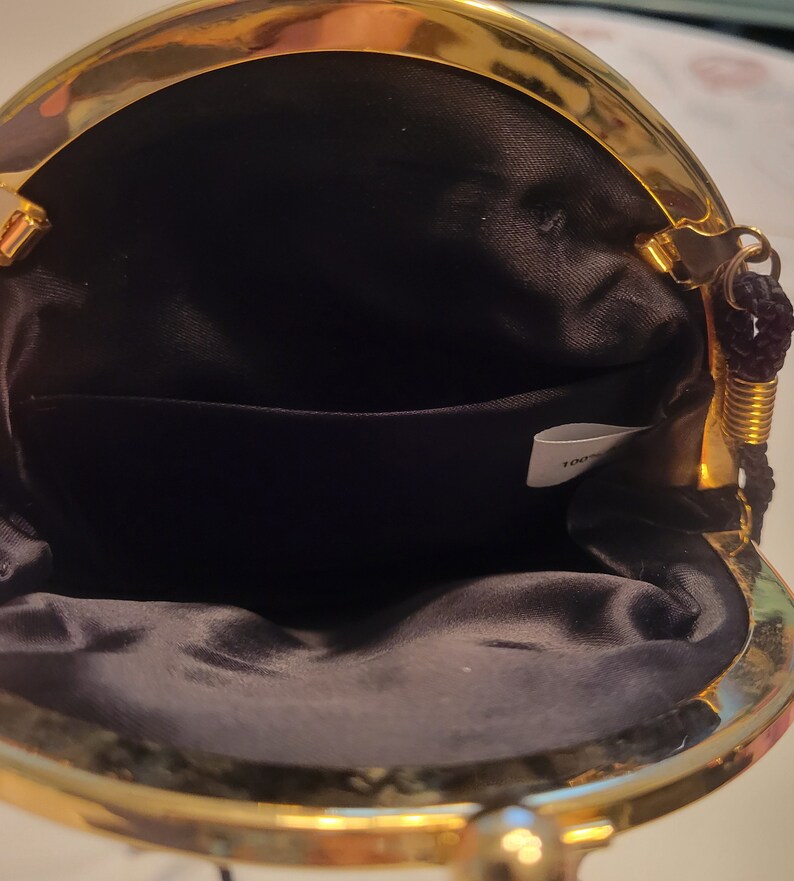 May include: Open view of a small, black satin purse with a gold-colored metal frame. The purse has a kiss-lock closure and a small interior pocket. A black cord handle is attached to the frame.