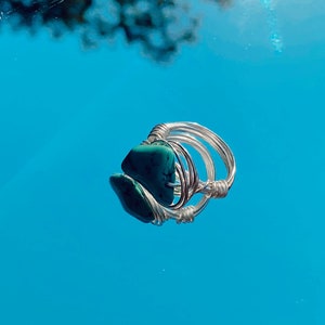 May include: A turquoise gemstone ring with silver wire wrapping. The ring is set against a blue background.