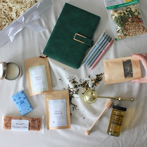 May include: A gift set with a green journal, pens, tea, honey, and a tea infuser. The set includes a bag of Frontier Soups Creamy Cauliflower Soup Mix, a bar of Cinnamon Toffee, and a small tin of lip balm.