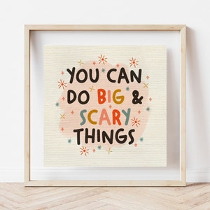Può includere: Una stampa incorniciata con uno sfondo acquerellato rosa e il testo "YOU CAN DO BIG & SCARY THINGS" in lettere nere, rosse, gialle e blu. Lo sfondo è decorato con piccole stelle e segni più.