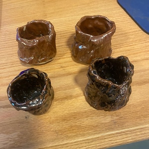 May include: Four small ceramic cups with a textured, tree bark-like design. Two cups are brown and two are black with brown accents.