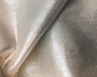 May include: Close-up of a silver fabric with a textured, sparkly finish. The fabric has a subtle sheen and a slightly bumpy surface.