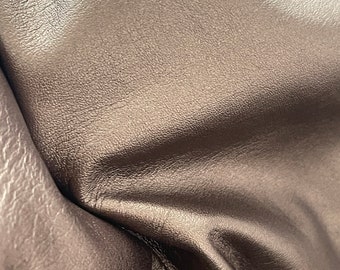 May include: Close-up of a brown leather material with a textured surface. The leather is folded and shows wrinkles and creases.