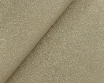 May include: A close-up of a folded piece of fabric. The fabric is a light beige color with a textured, speckled surface. The fold creates a diagonal line across the image, revealing the underside of the fabric.