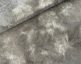 May include: Close-up of a silver metallic fabric with a textured, pebbled surface. The fabric has a subtle sheen and a slightly distressed look.