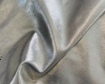 May include: A close-up of a silver metallic fabric with a textured surface. The fabric is folded and has a soft, smooth feel.